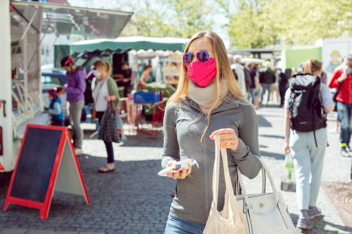 a woman shops at a farmers market with a mask on
