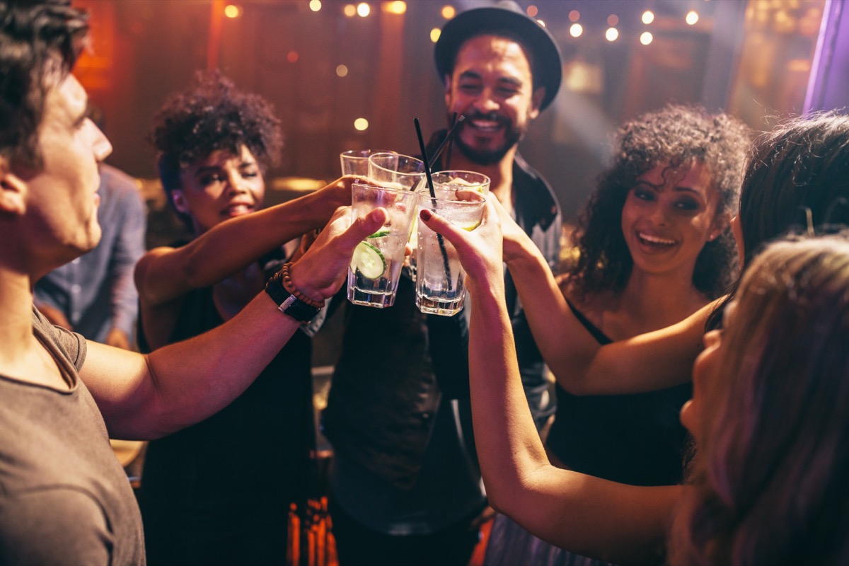 Grup de prieteni care beau băuturi la o petrecere în club de noapte.  La bar, tinerii se bucură de prăjire de cocktailuri.