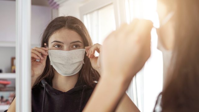 young girl wearing medical protective face mask looking mirror stay at home social dictancing concept