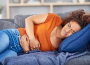 young woman clutching her stomach in pain while lying on the couch