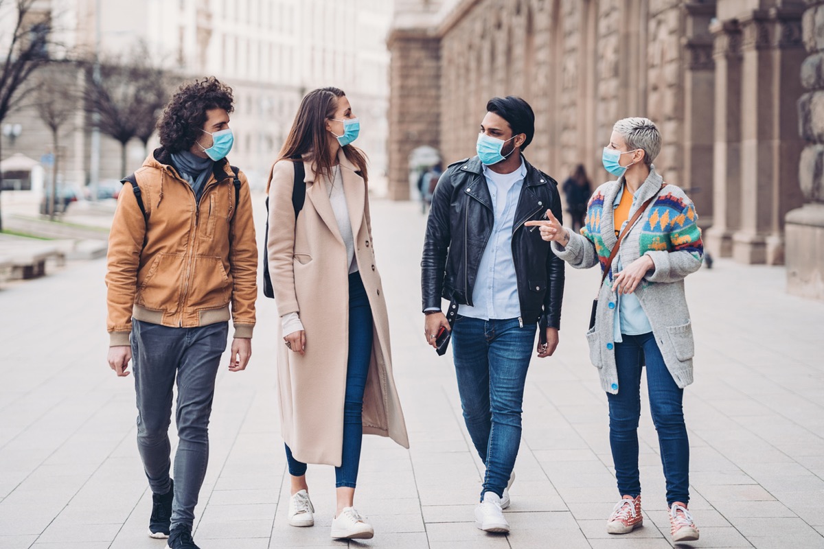 four friends wearing face masks walking down a city street
