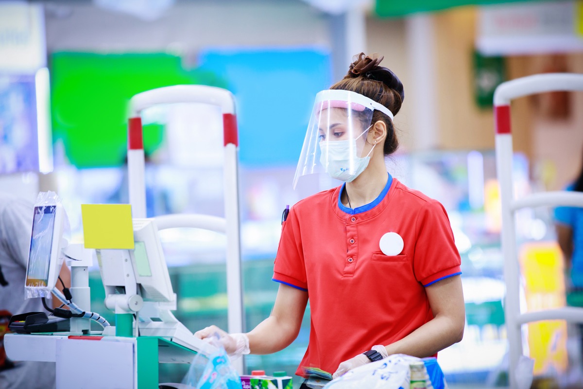 female supermarket cashier wearing a face mask and a face shield