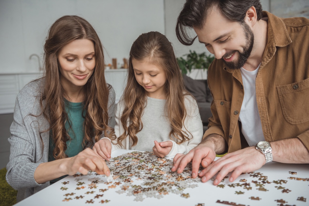 happy parents and daughter connecting puzzle pieces at table