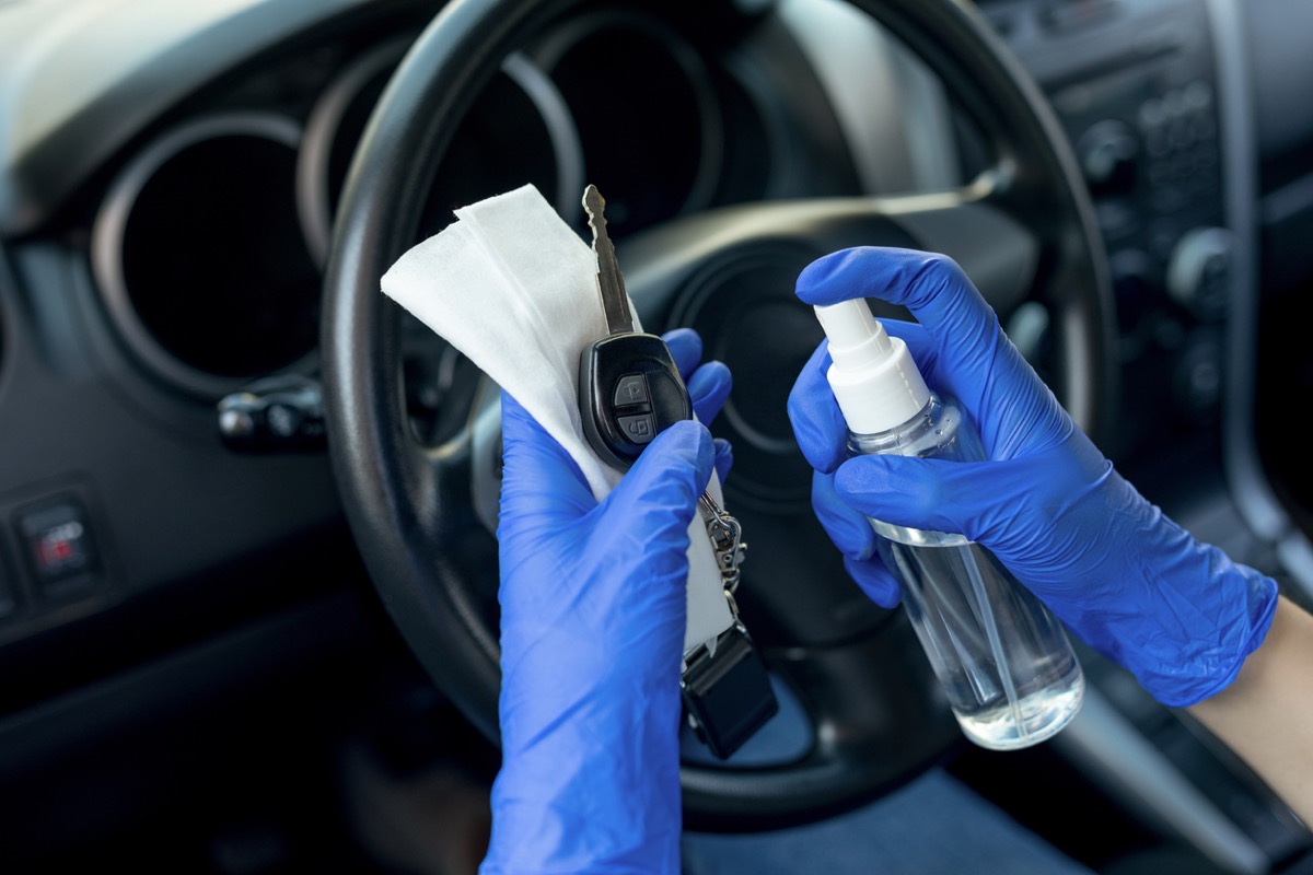 Disinfecting car key with gloved hand over wheel