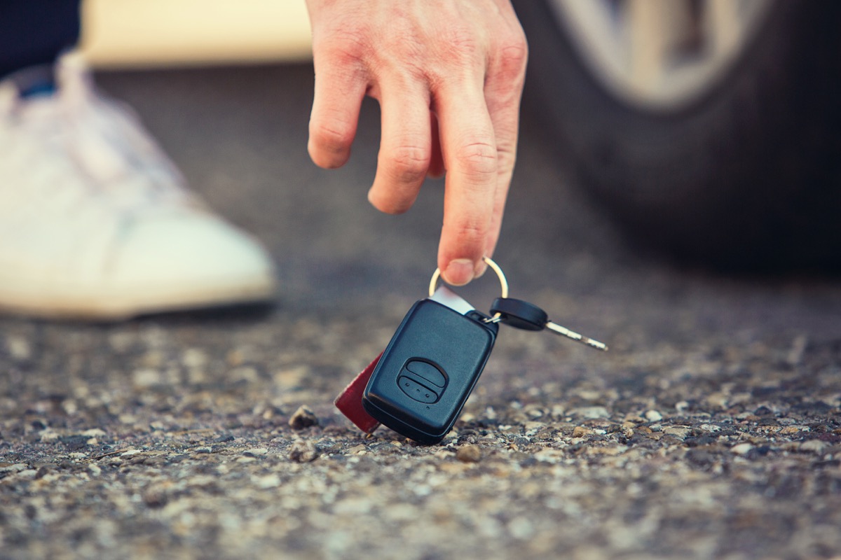 Close up of man hand lifting car keys fallen on the ground. Guy found vehicle keys someone lost on the asphalt road in the parking. Return property to owner.