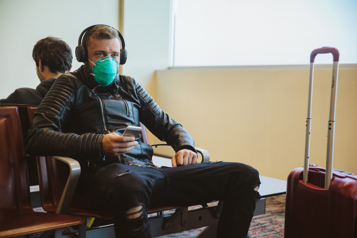 young white man sitting at airport wearing face mask