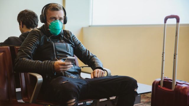young white man sitting at airport wearing face mask