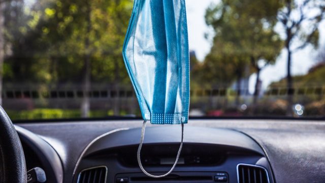A disposable medical mask is hung on the front of the car