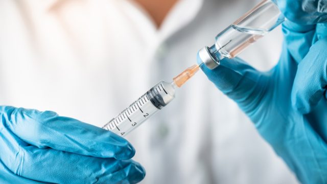 scientist wearing blue gloves holding vaccine vial