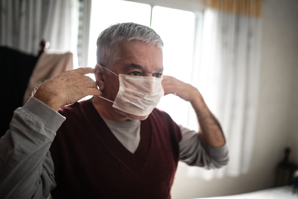 Senior man putting on a protective mask for coronavirus at home