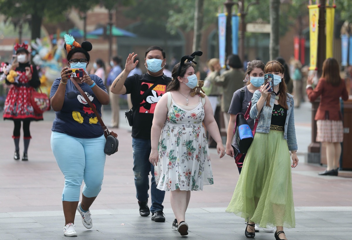 a group of people in masks walk on main street in shanghai disneyland