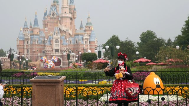 girl in disney outfit takes a selfie in front of the castle