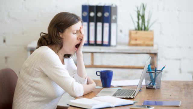 Woman yawning at her desk in front of a laptop