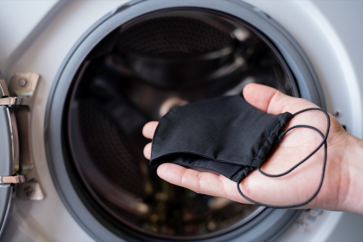 The hand of a man who is throwing a black mask into the washing machine