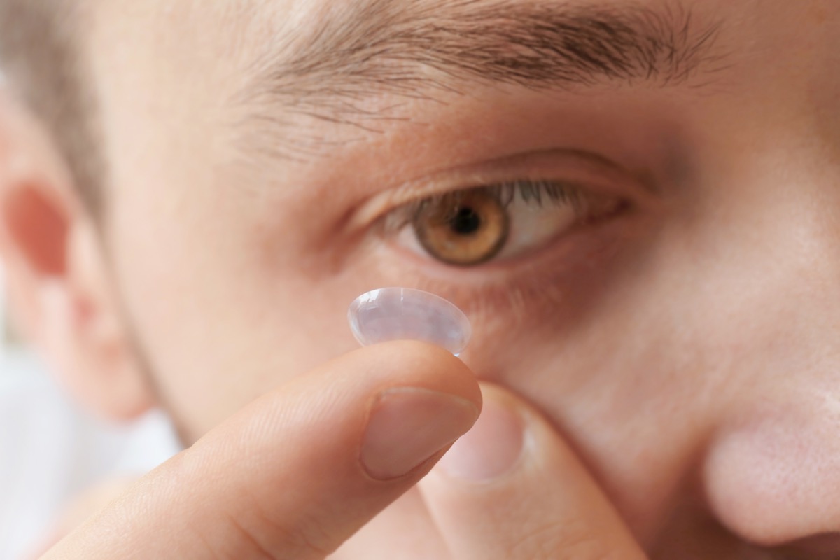 white man putting contact lens in eye