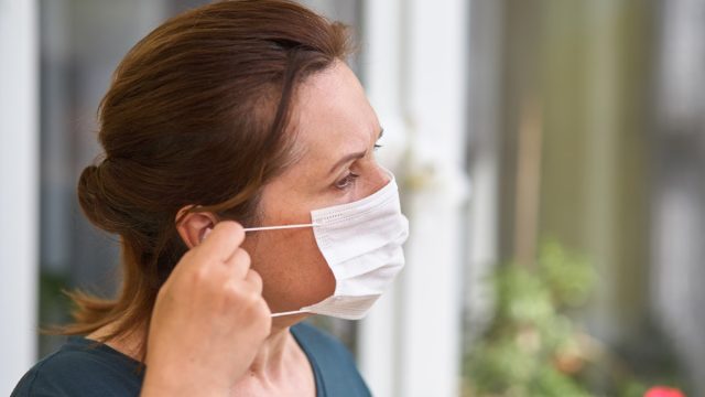 middle aged white woman putting on disposable face mask