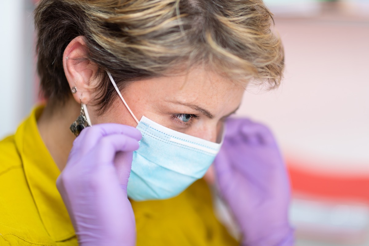 Woman wearing protective gloves putting on protective mask on her face at work place