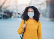 a young woman in a yellow sweater wearing a surgical mask
