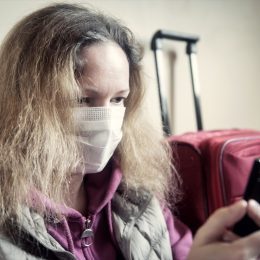 woman looking at smartphone sitting next to suitcase