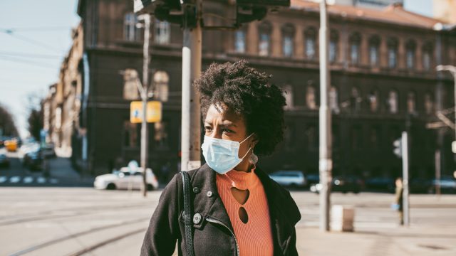Young black woman standing on city street with protective mask on her face