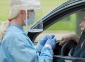 White female nurse in face shield testing mature white man in car for coronavirus