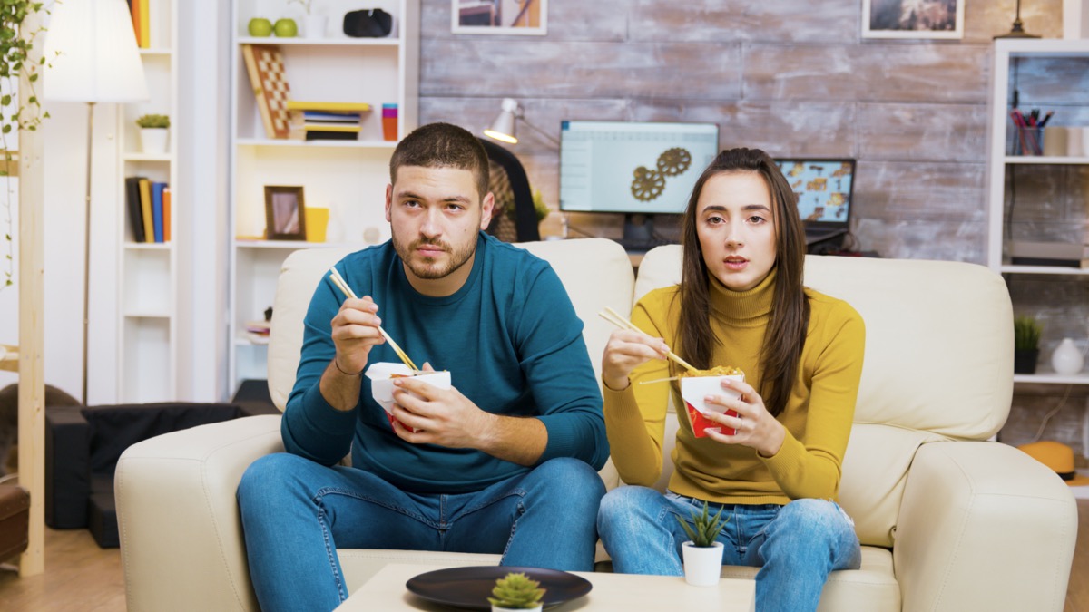 Couple sitting on couch and eating Chinese food