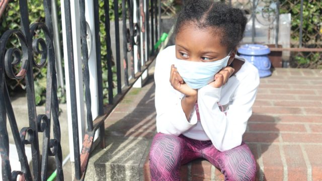 Young black girl wearing mask sitting on steps