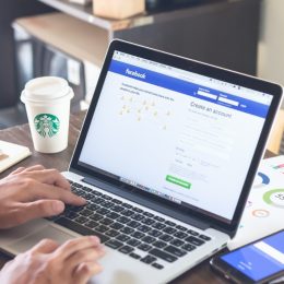 Person logging into Facebook on laptop at coffeeshop