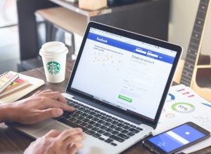 Person logging into Facebook on laptop at coffeeshop
