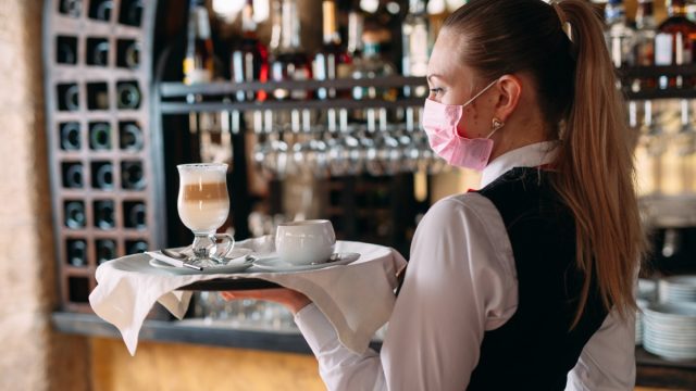 Young white waitress wearing mask and carrying tray in restaurant