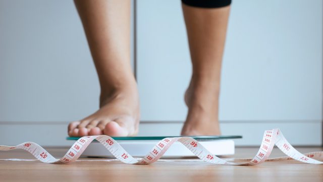 Woman stepping on scale with measurement tape