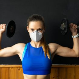 Young white woman lifting weights and wearing a mask