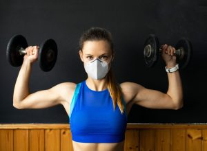 Young white woman lifting weights and wearing a mask