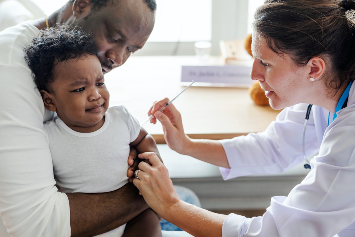 black baby with father getting vaccine from white female doctor