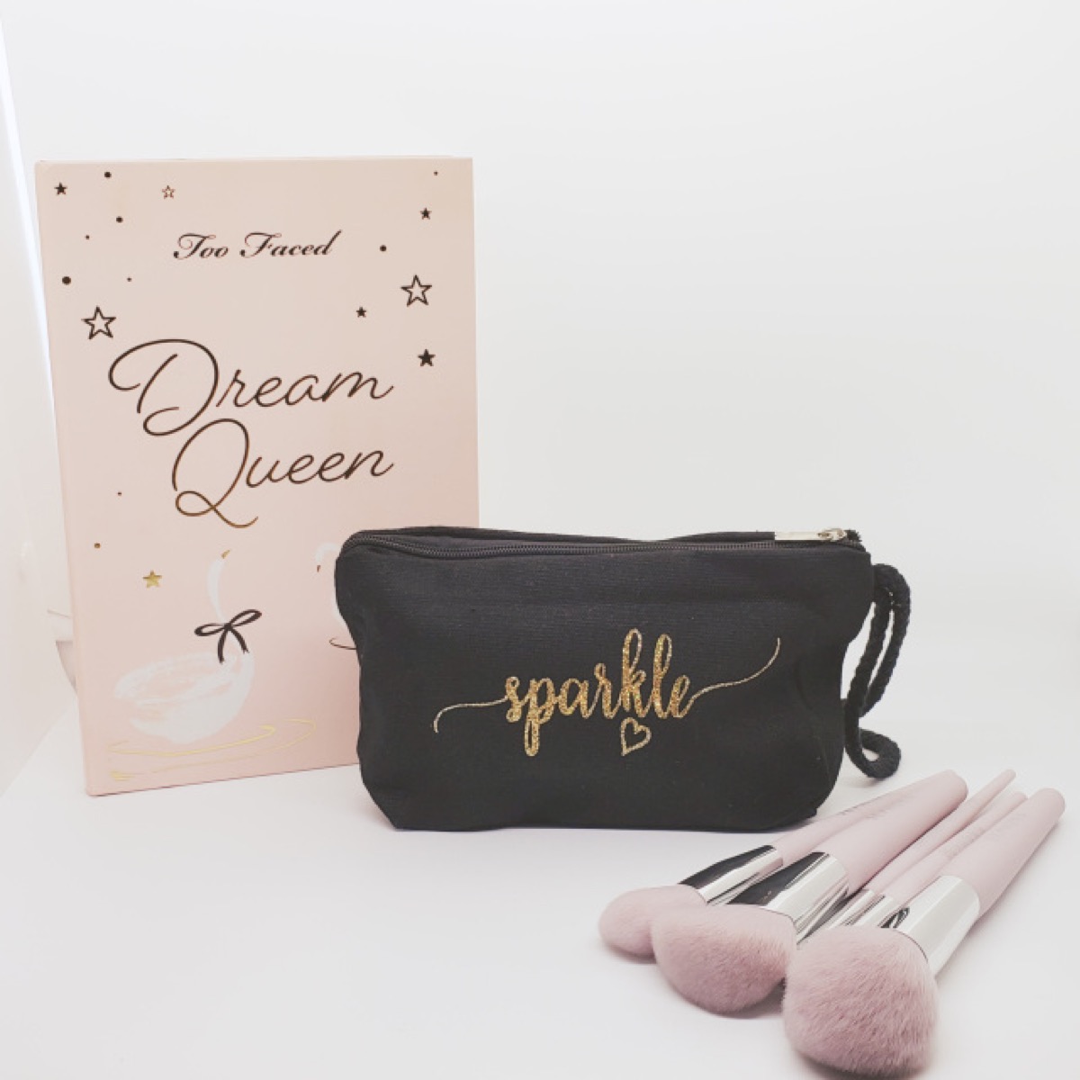 black cosmetics bag that says sparkle next to makeup brushes