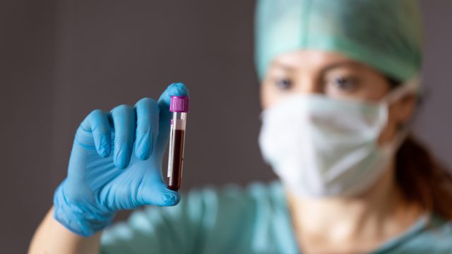 A female Asian doctor holds up a test vile of blood