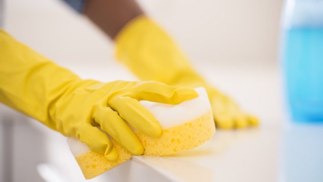 Unrecognized women cleaning the kitchen, using yellow protective gloves, blue spray bottle and cleaning rag.