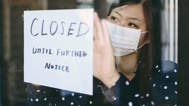 An Asian woman wearing a face mask putting up a "closed until further notice" sign