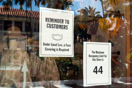 Two signs in a store window limiting occupancy to 44 and requiring a face mask.