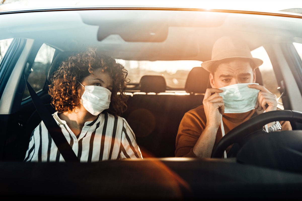 Coronavirus pandemic concept. breathing through a medical mask because of the danger of getting the flu virus, influenza infection. Enjoying travel. Beautiful young couple sitting on the front passenger seats and smiling while handsome man driving a car