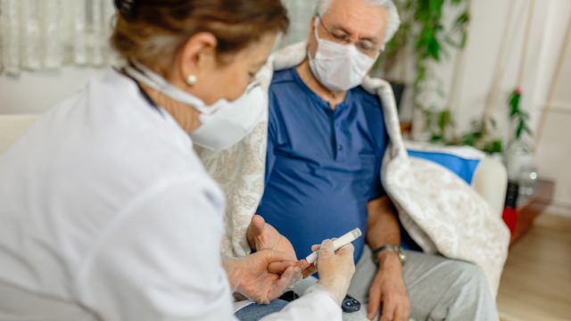 man gets blood sugar levels checked by nurse, both wear masks