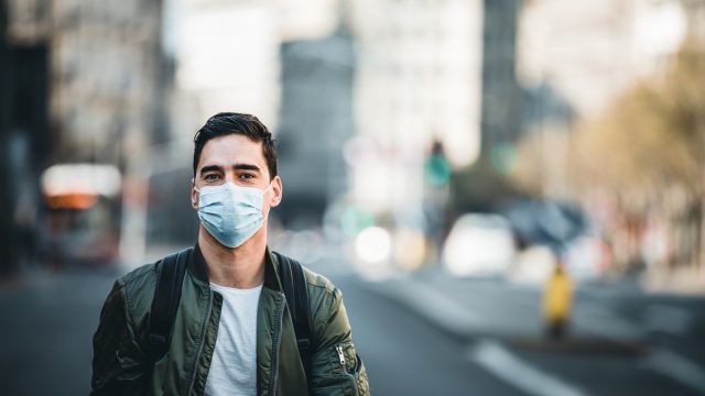 Concept, diseases, viruses, allergies, air pollution. Portrait of young man wearing a protective mask, walking in the city.The image face of a young man wearing a mask to prevent germs, toxic fumes, and dust. Prevention of bacterial infection Corona virus or Covid 19 in the air around the streets and gardens.