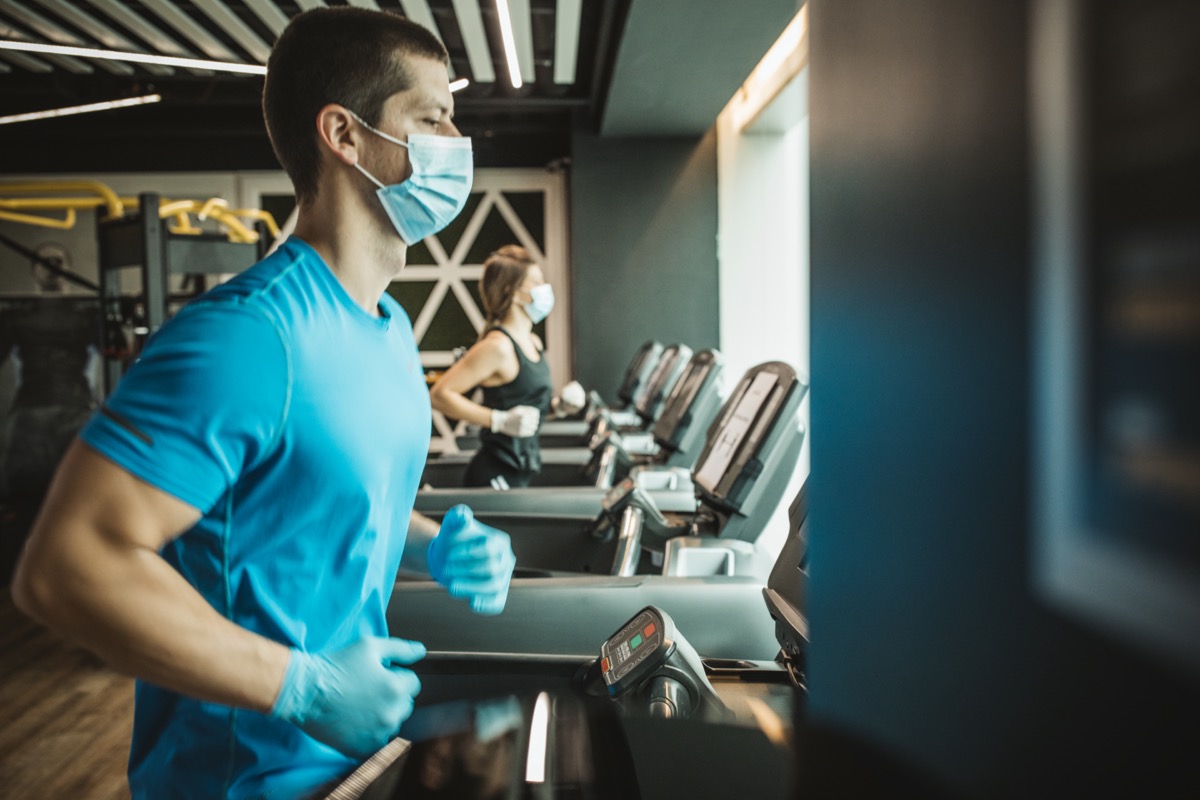man and woman use treadmills at a gym with masks on