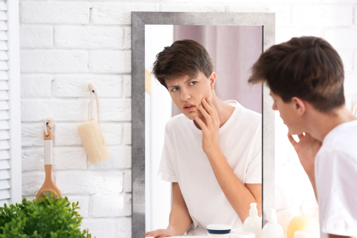 young man examining face in mirror