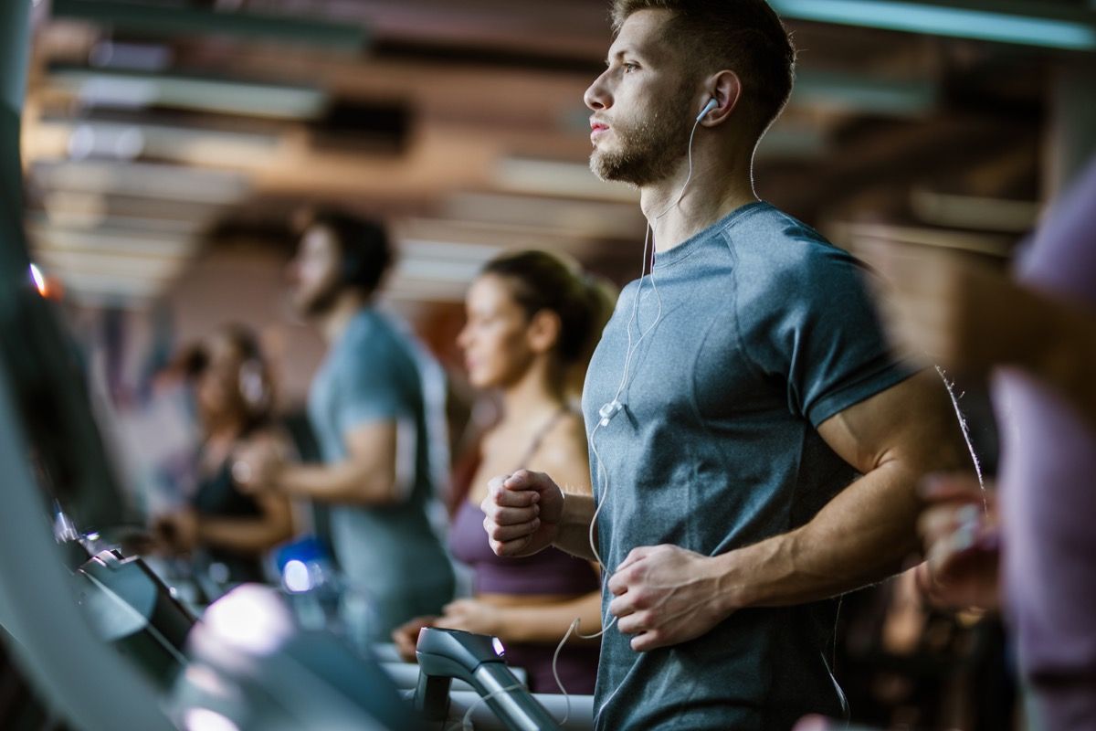 Young male athlete listening music while exercising on treadmill in a gym.