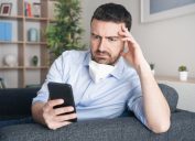 Worried man at home reading phone with mask no chin amid coronavirus