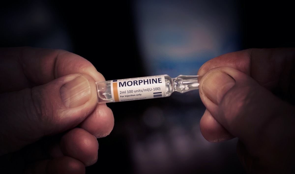 white hands holding glass vial of morphine painkiller