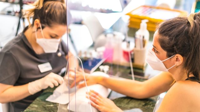 woman getting a manicure through a shield at a nail salon