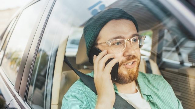 Young Man Riding on a Passenger Seat of a Car Makes a Phone Call, Talks with Clients, Customers and Business Associates. Camera Shot from Outside the Vehicle.