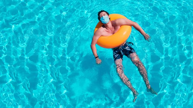 man lays in pool in inner tube while wearing a mask amid coronavirus